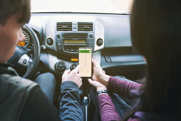 导航一对年轻人开着车 看着智能手机上的gps应用程序情侣地图驾驶