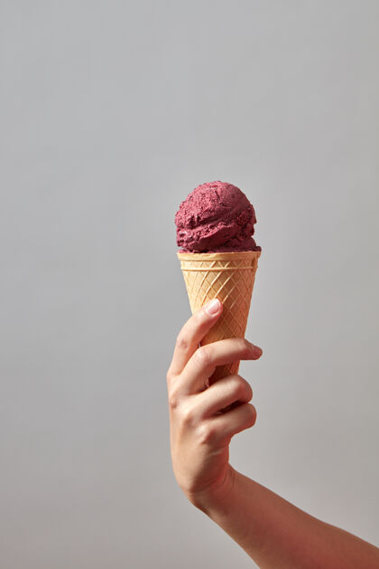 球华夫饼筒里的浆果冰淇淋一个女孩的手在灰色的墙上拿着一个冰淇淋冰冷的液体