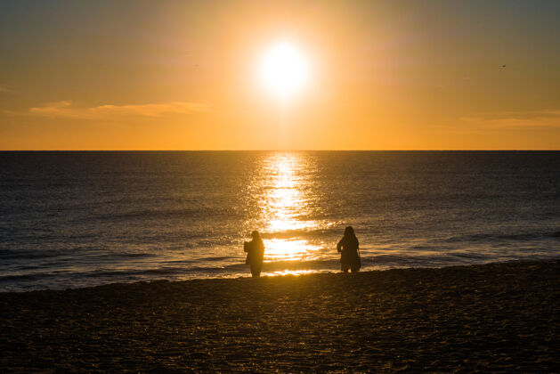 日落日落在海滩与太阳在天空中 两个人在剪影波浪美丽海洋