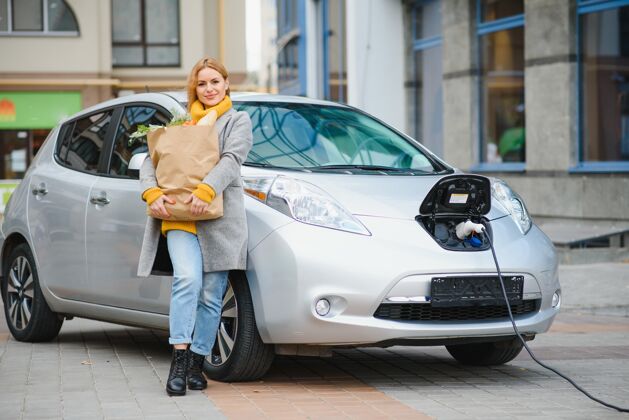 发动机时尚女士买完产品后拿着购物袋正站在充电的电动车旁环保公园电力