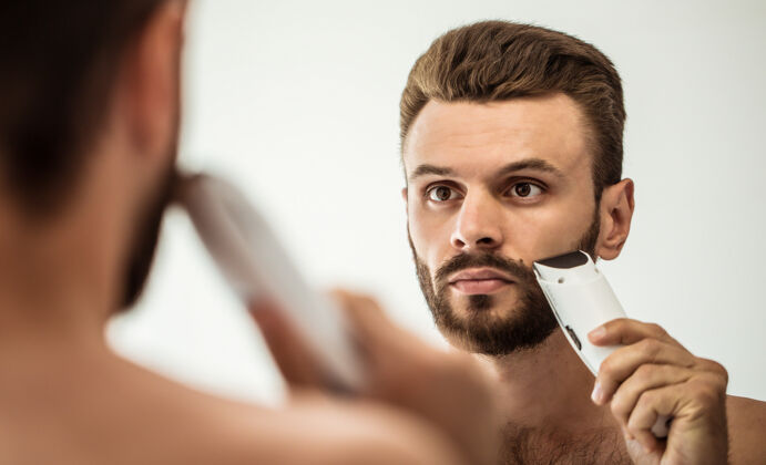 反射英俊的年轻人在街上刮胡子浴室.肖像一个时髦的裸体胡须男人在家里的镜子里检查他的脸发型胡须肌肉