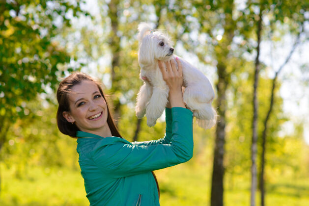 玩耍年轻女人和她在一起狗小狗白狗正和它的狗一起跑业主概念关于友谊和动物散步健身公园
