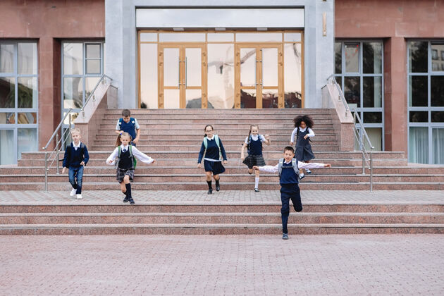 教育一群穿着制服的小学生从学校的楼梯上跑下来水平小学高尔夫