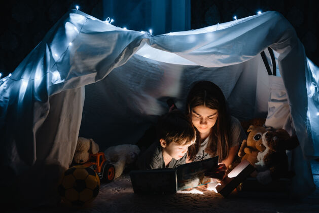 童年幸福家庭母子俩在帐篷里用手电筒看书主页.家庭概念教育白天小