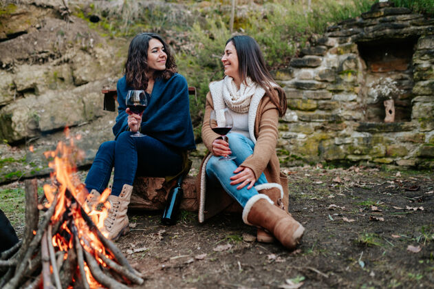 欢呼年轻快乐的女人一边喝酒一边聊天葡萄酒女性温暖的天气篝火户外活动概念篝火酒在一起