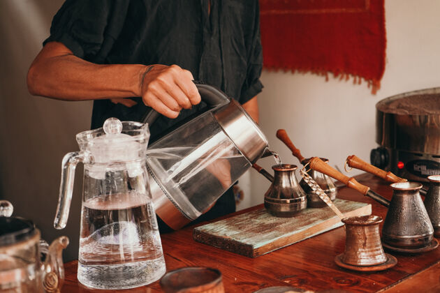 热一个女人把开水倒进锅里杯子咖啡师在桌子上准备咖啡沙子传统的咖啡准备女人餐馆热