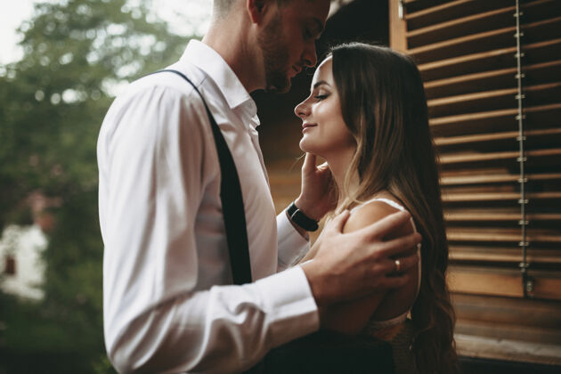男性一个可爱的年轻新娘在新郎亲吻她的额头时被新郎拥抱的侧视图西装拥抱庆典