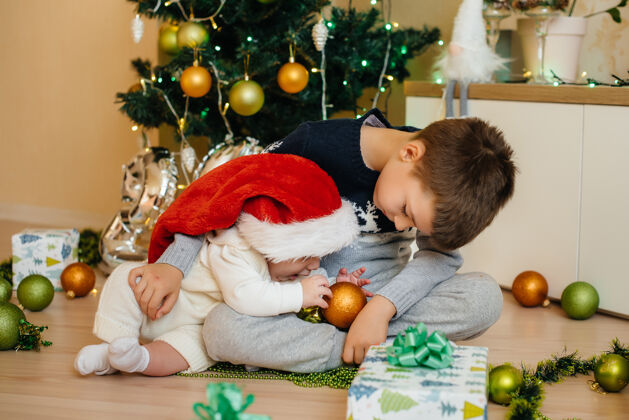 脸一个小男孩和他的弟弟在圣诞树下玩礼物装饰圣诞树可爱