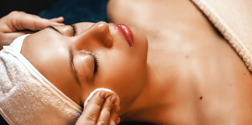 清洁与一位躺在专业水疗沙龙的年轻女子进行面部按摩敏感治疗皱纹