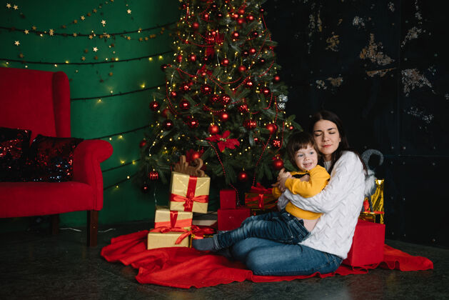 盒子年轻美丽的母亲带着可爱的儿子在圣诞树旁礼物快乐圣诞节女孩儿子圣诞树
