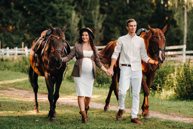 肥料在大自然的森林里 一个戴着帽子的孕妇和她穿白色衣服的丈夫站在马旁边马等待怀孕