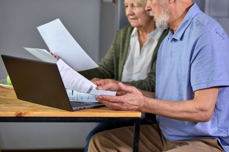 退休不规则的老人和女人一起管理家庭每月的预算 专注于已婚夫妇使用电脑银行应用程序 计算账单厨房焦点在笔记本电脑和手上老人会计笔记本电脑