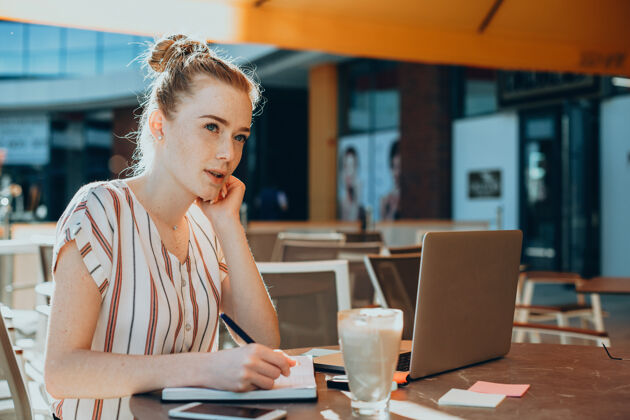 信息一个可爱的年轻女性自由职业者在咖啡馆户外工作时的侧视图数码笔记本电脑社交媒体