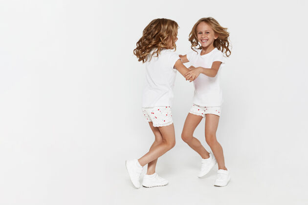 年轻笑容可掬的穿着白色衣服的双胞胎小姐妹在跳舞童年小白布孩子