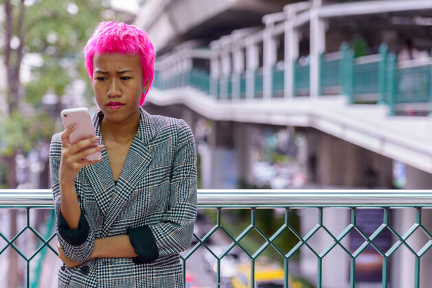 天桥年轻叛逆的亚洲女商人的肖像 粉红色的头发在城市户外的人行天桥上手机酷20多岁