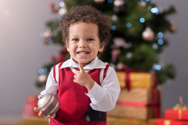情感准备太可爱了可爱的快乐男孩站在圣诞树前微笑着拿着圣诞装饰品期待庆祝当代