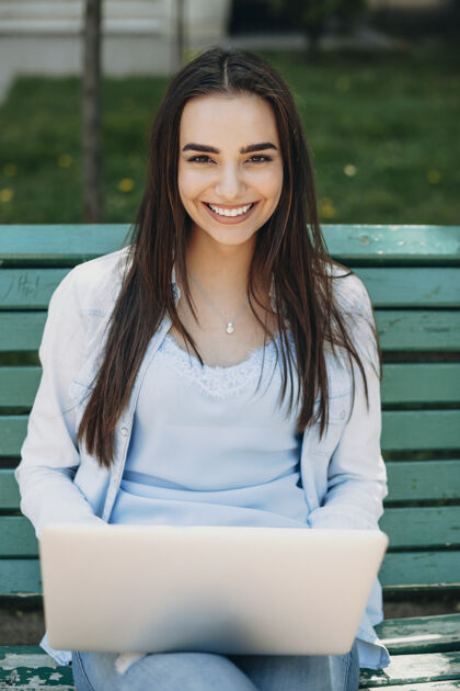 在线一个惊人的长发黑发女子坐在沙滩上用笔记本电脑对着相机笑的照片学生电脑微笑
