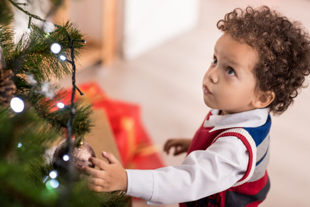 腰部以上怎样漂亮不错可爱体贴的孩子站在圣诞树旁 一边看着圣诞树 一边抚摸着圣诞树的装饰光魅力童年