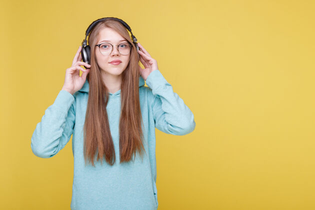 小玩意戴着耳机的女孩在黄色背景上听音乐音乐科技耳机