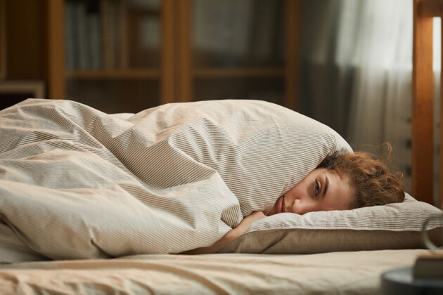 睡眠躺在床上毛毯下的年轻女子的画像她感到很不舒服疾病悲伤肖像
