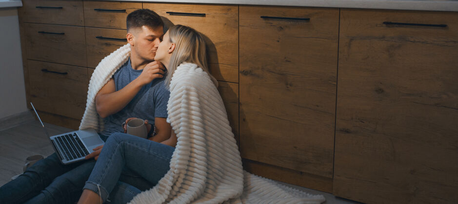舒适美丽的年轻夫妇下班后坐在厨房的地板上亲吻拥抱女人拥抱年轻