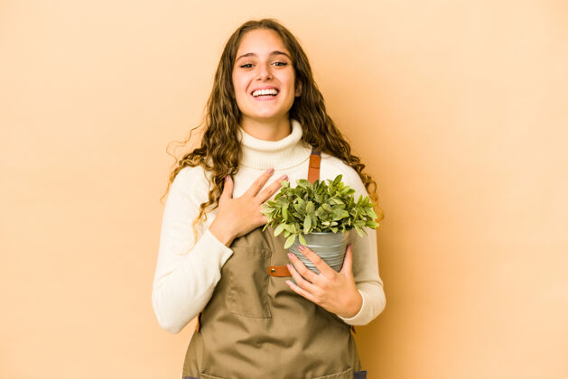 嘲笑年轻的高加索园丁女人拿着一株孤立的植物大声笑出来 手放在胸前主人年轻乐观