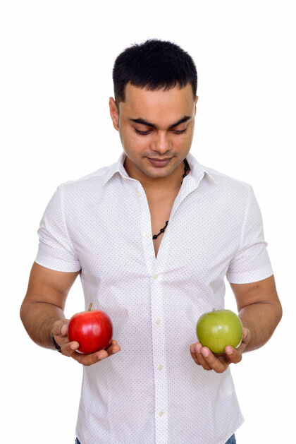 选择年轻英俊的印度男人拿着红绿相间的苹果隔离在白色的空间里决定镜头20多岁