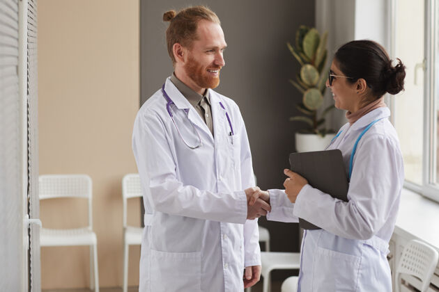 工作身穿白大褂的医生和护士站在医院里互相握手微笑实验室外套谈话表情
