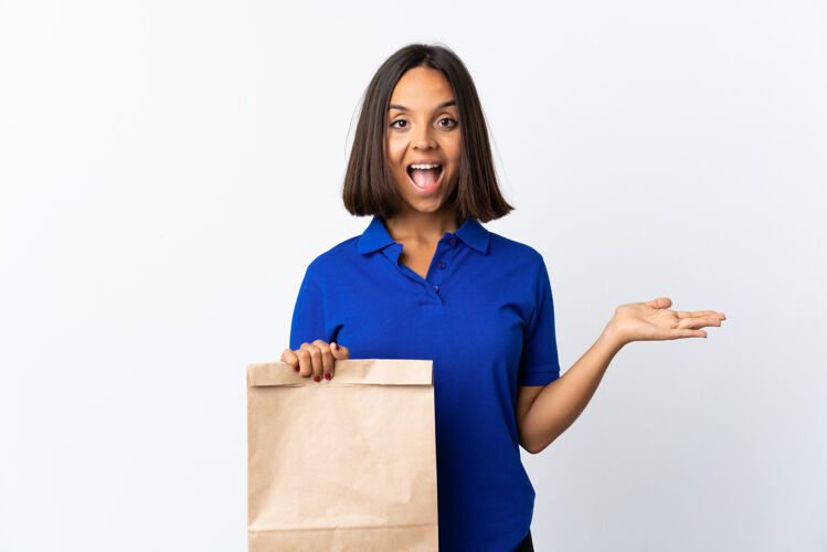 好一个年轻的拉丁女人拿着一个杂货店的购物袋 脸上的白色与震惊的表情隔离食物商店手势
