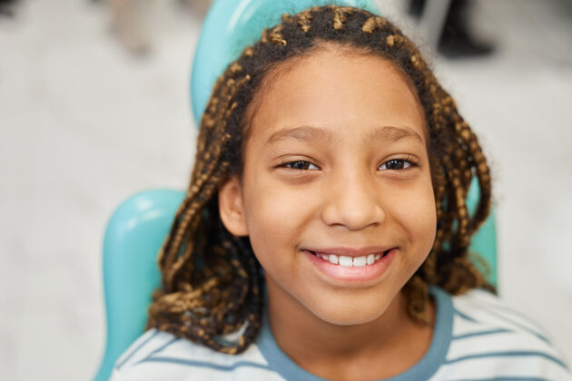 休闲服坐在牙科手术椅上的快乐小女孩微笑在前面的特写镜头童年小学年龄青春期前的孩子