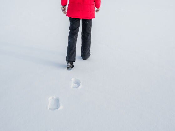 脚穿着红色夹克的女人在雪地上行走 脚印在雪地里 在身后剪影运动天气