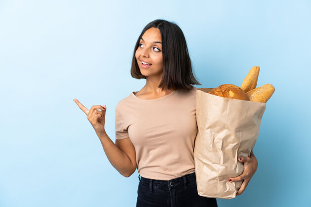 年轻一个年轻的拉丁女人在买一些孤立于蓝色的面包 想在举起一根手指的同时实现解决方案女人赛车成人