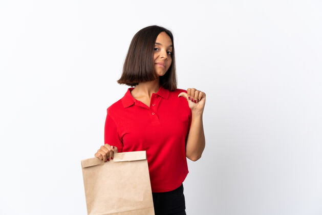 混合年轻的拉丁女子拿着一个杂货店的购物袋孤零零地站在白色的骄傲和自满上杂货店食物胜利