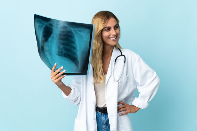 制服年轻的金发乌拉圭女医生孤立的蓝色摆出双臂在臀部和微笑医疗医疗保健从业者