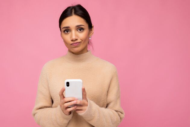 设备迷人可爱不快乐的年轻黑发女子穿着米色温暖毛衣站着年轻手机用户