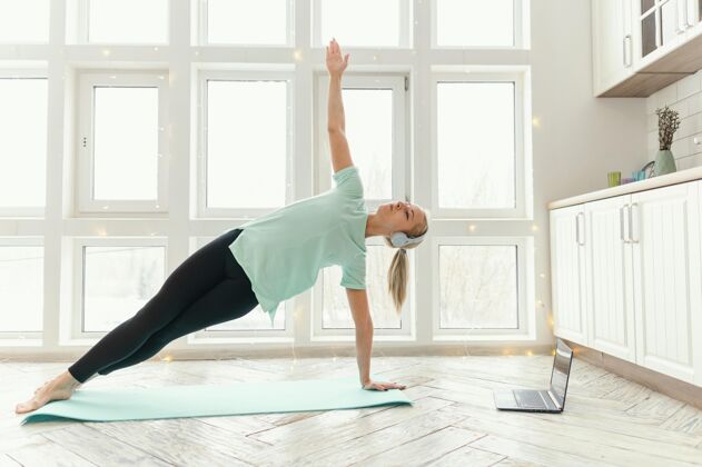 耳机女性在垫子上锻炼 在笔记本电脑上看视频运动瑜伽垫房子