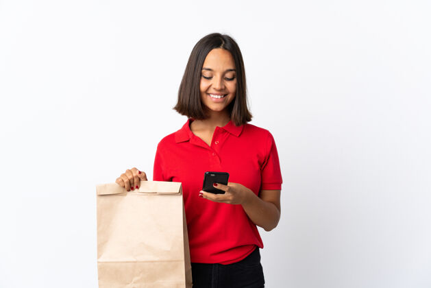 食品年轻的拉丁女子拿着一个杂货店购物袋 用手机发信息控股青年赛车