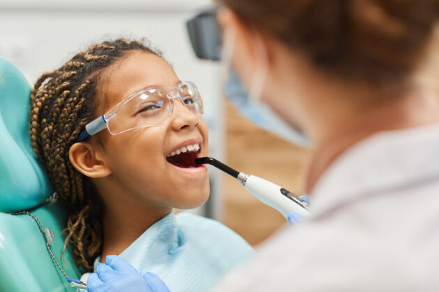 工作戴着护目镜的小女孩在医院看牙医治牙时张嘴举行看室内
