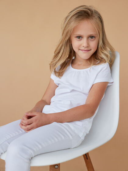 工作室前面的特写照片是一个美丽的微笑的小女孩 卷曲的金发 穿着白衣服 坐在椅子上女孩时尚金发