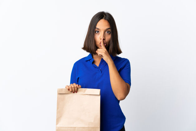 市场一个年轻的拉丁女人拿着一个杂货店的购物袋 在白色的地板上显示出沉默的手势 把手指放进嘴里深色消费者购买