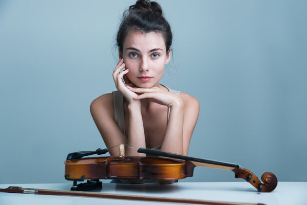 年轻人一个美丽的年轻女子坐在桌子旁 小提琴孤立在蓝色背景下的肖像一小提琴手高加索