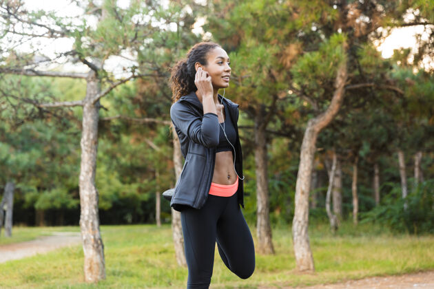 户外20多岁的非洲裔美国妇女穿着黑色运动服热身 在绿色公园伸展身体的画面女性听户外