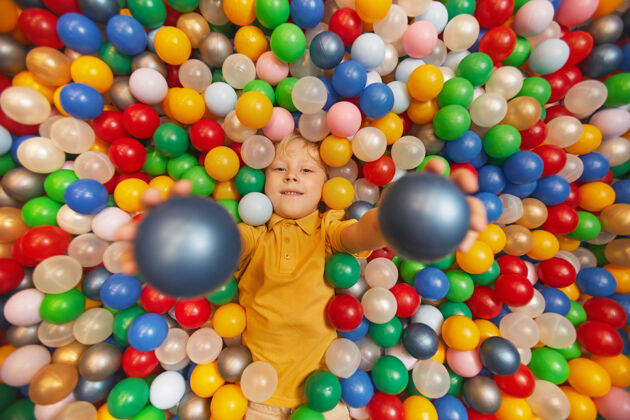 可爱快乐的孩子躺在彩球中间 把球扔上去的画像童年塑料鲜艳的颜色