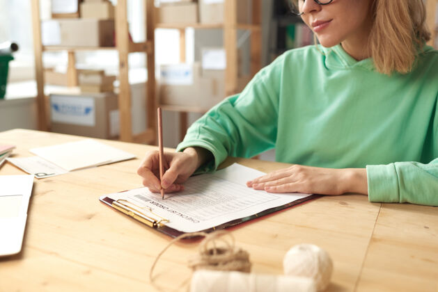 工作坐在桌边 在文件里写计划的年轻女子的特写镜头写作商务女士成人