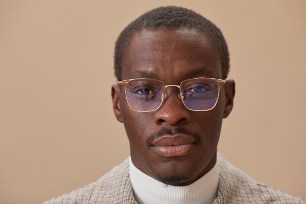 商务一个戴着眼镜的年轻优雅的男人在米色的墙上看前面的特写镜头眼镜站立特写