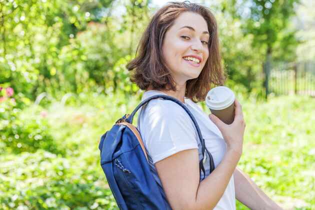 回来快乐积极的女学生 背着背包 在绿色公园的背景下微笑着背景旅行女孩