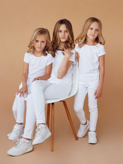 孩子三个身着白色衣服的金发卷发姐妹的全长图像垂直视图可爱女孩年轻