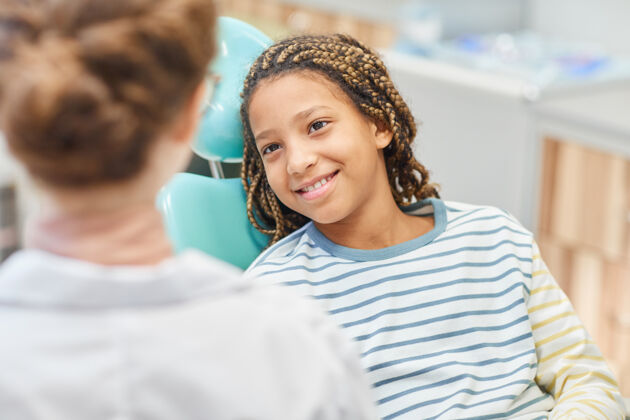 孩子微笑的小女孩坐在牙科椅上和医院的医生交谈肖像微笑牙医办公室