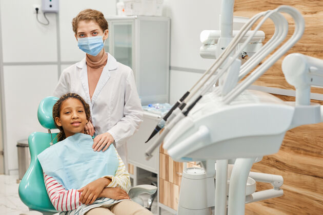 牙科办公室戴着面具的护士站在诊所牙科手术椅上看病人旁边的画像护士助理外科面罩