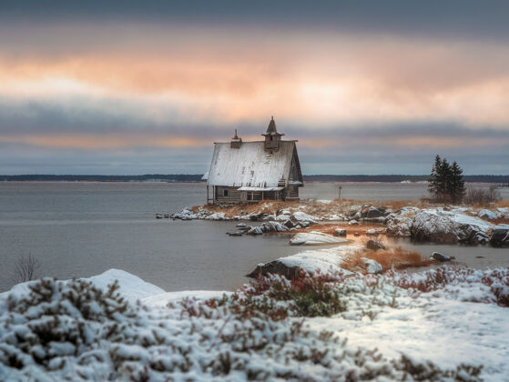 北极波美拉尼亚的神奇日落村庄下雪冬季风景与真实的房子在俄罗斯拉博乔斯托罗夫斯克村岸边降雪极简主义小教堂